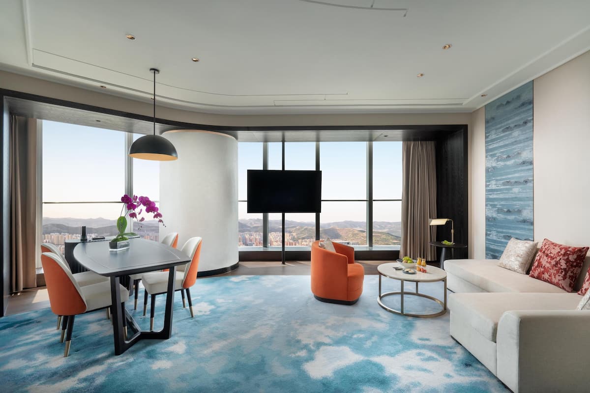 Une chambre d’hôtel moderne dotée d’un coin repas, d’un canapé, d’une télévision et d’une grande fenêtre offrant une vue sur la ville.