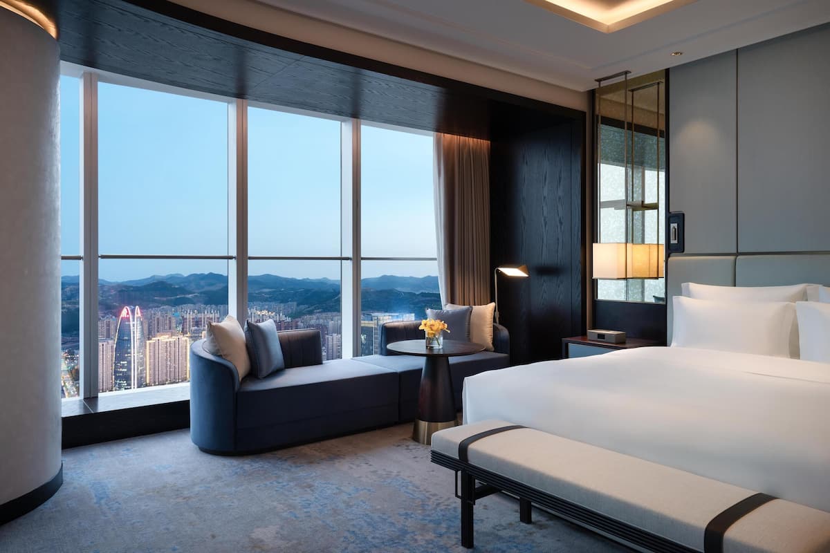 Une chambre d’hôtel moderne dotée d’un grand lit, d’un coin salon avec vue sur la ville et d’une grande fenêtre.