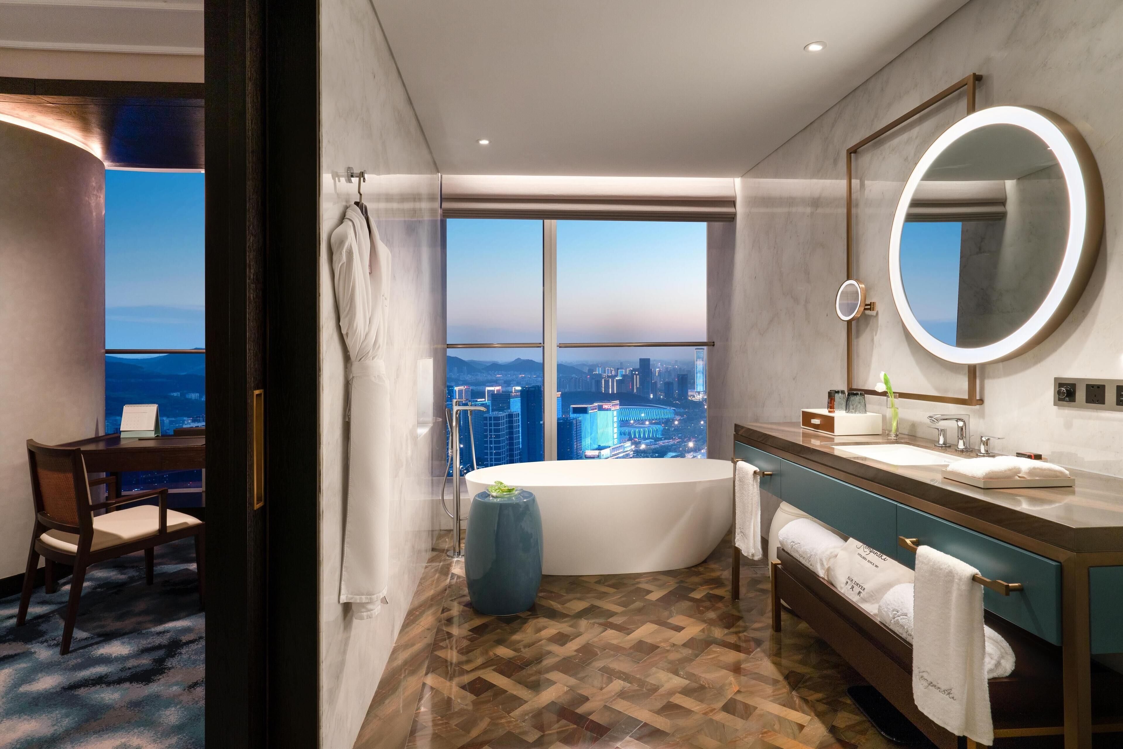 A modern bathroom with a large bathtub, a vanity with a mirror, and a view of the cityscape through large windows.