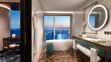 A modern bathroom with a large bathtub, a vanity with a mirror, and a view of the cityscape through large windows.