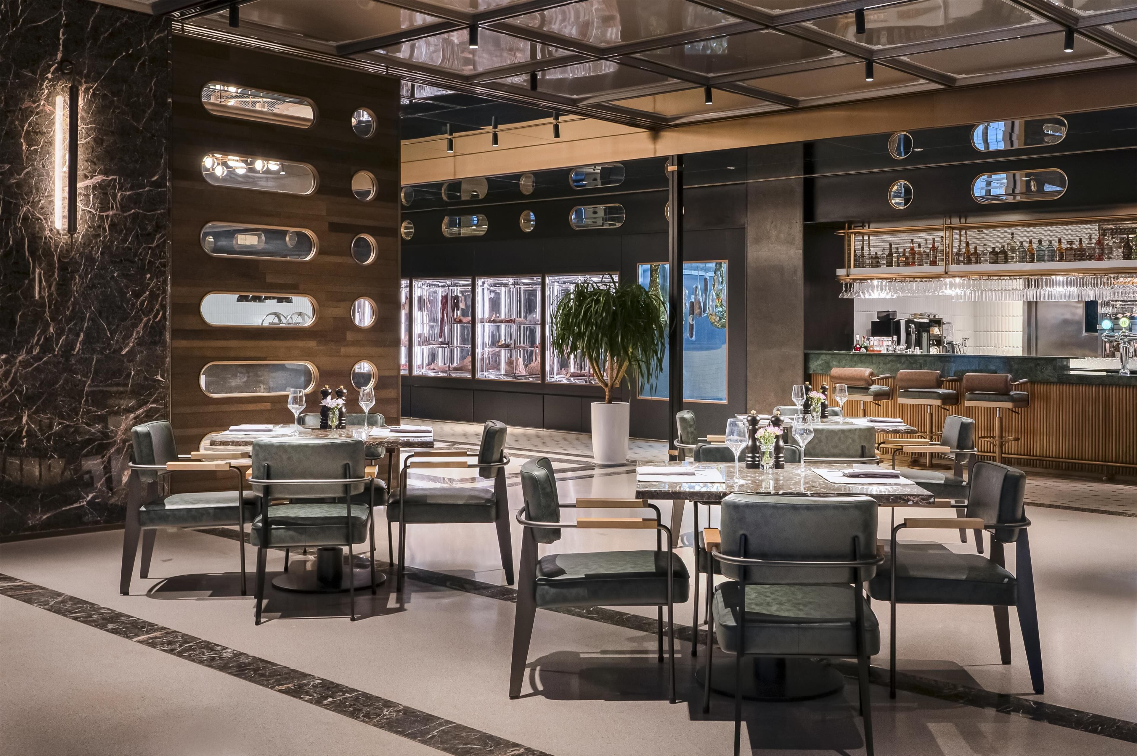 Un restaurante moderno con paredes de mármol, varias zonas de estar y una barra con una amplia variedad de botellas.