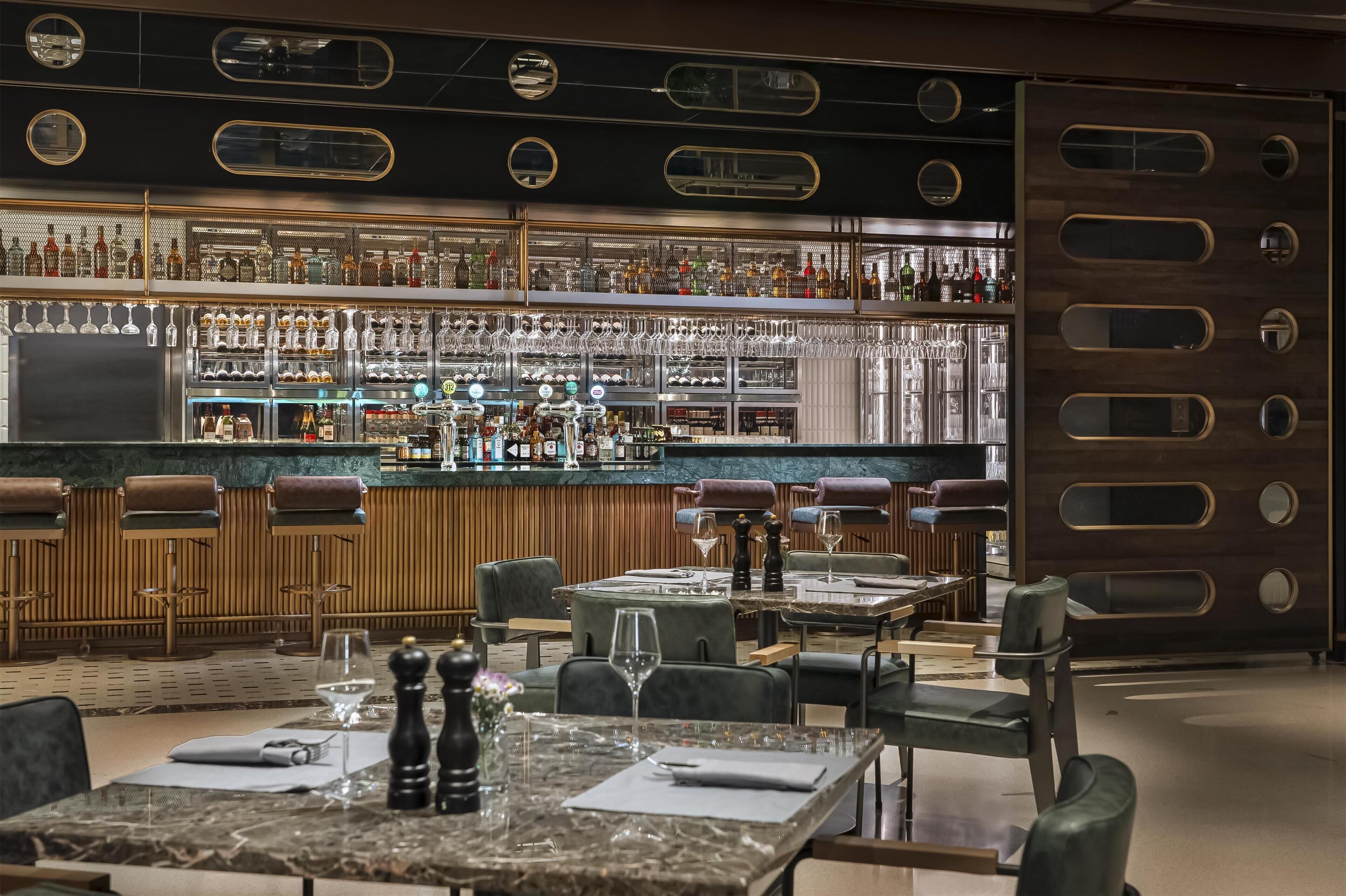 Un espace bar comprenant un assortiment de bouteilles d’alcool et de verres, des comptoirs en bois et des sièges pour les clients.