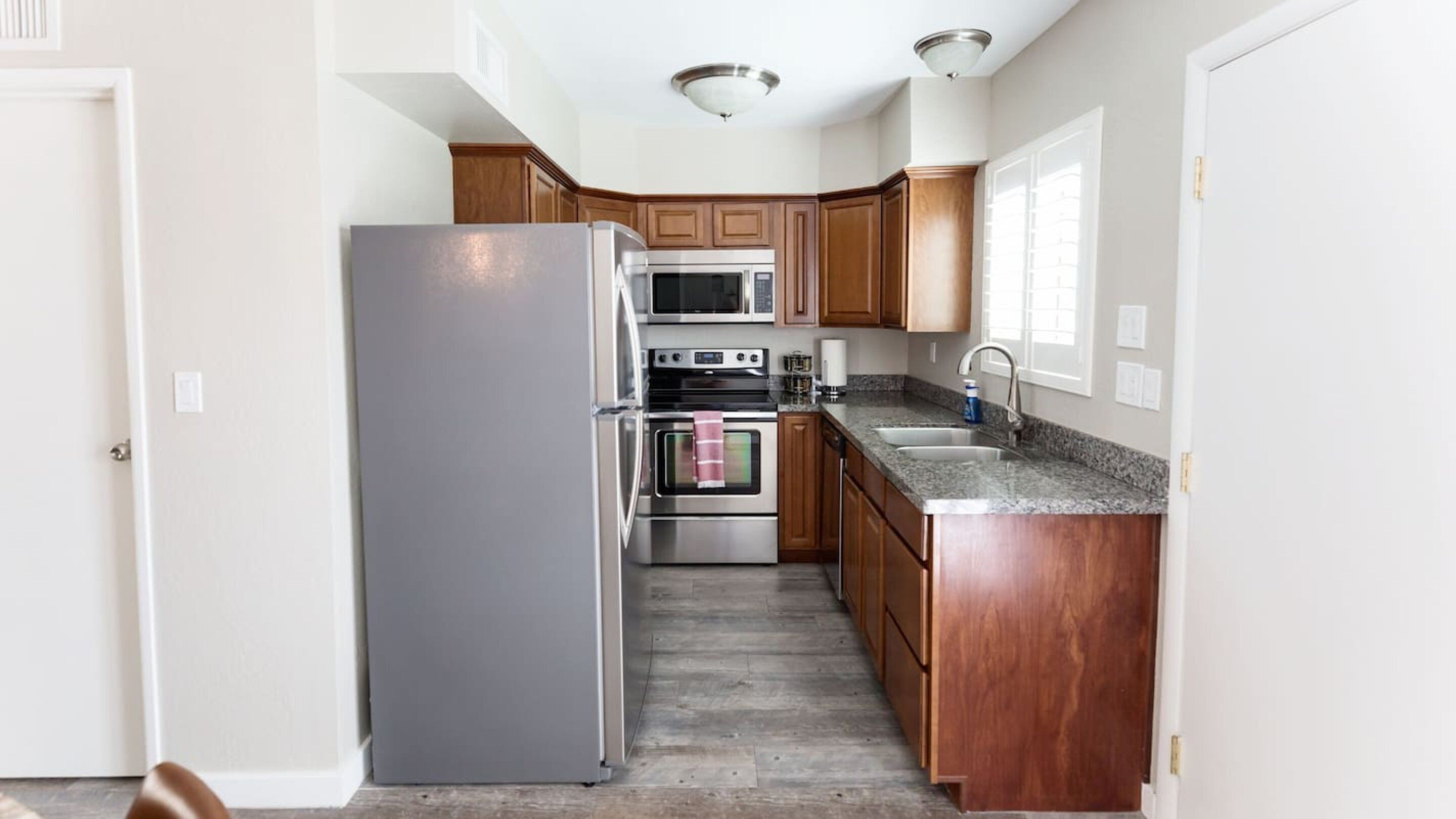 A kitchen with wooden cabinets, stainless steel appliances, a granite countertop, and a tiled floor.