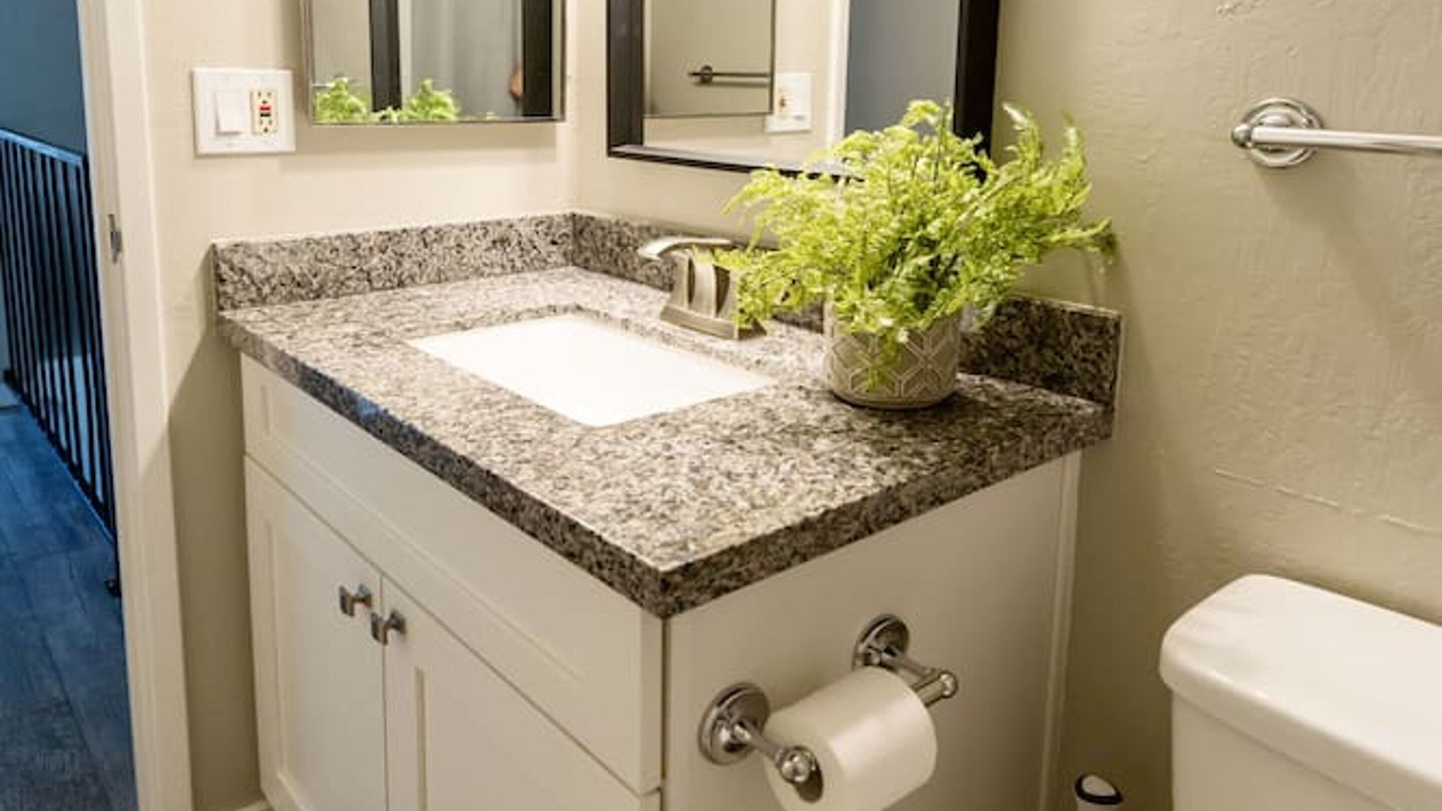 A bathroom with a granite countertop, a white sink, a toilet, and a mirror above the sink.