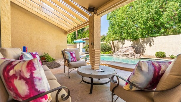 Ein überdachter Patio-Bereich mit Pool, Gartenmöbeln und Blick auf die umliegende Landschaft.