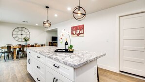 Une cuisine moderne dotée d’un grand îlot central, de meubles blancs et d’un coin repas avec une table et des chaises en bois.