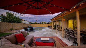 Une terrasse extérieure avec une piscine, un espace salon couvert et des guirlandes lumineuses.