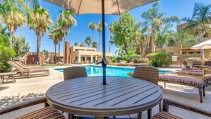 A poolside area with lounge chairs and a table, surrounded by palm trees and buildings. - Stylish Old Town 2 Bdrm Ground Floor Condo (Scottsdale)