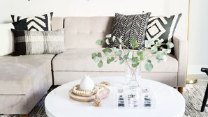 A modern living room with a beige sofa, patterned cushions, a white coffee table, and a vase with green leaves. - Stylish Old Town 2 Bdrm Ground Floor Condo (Scottsdale)