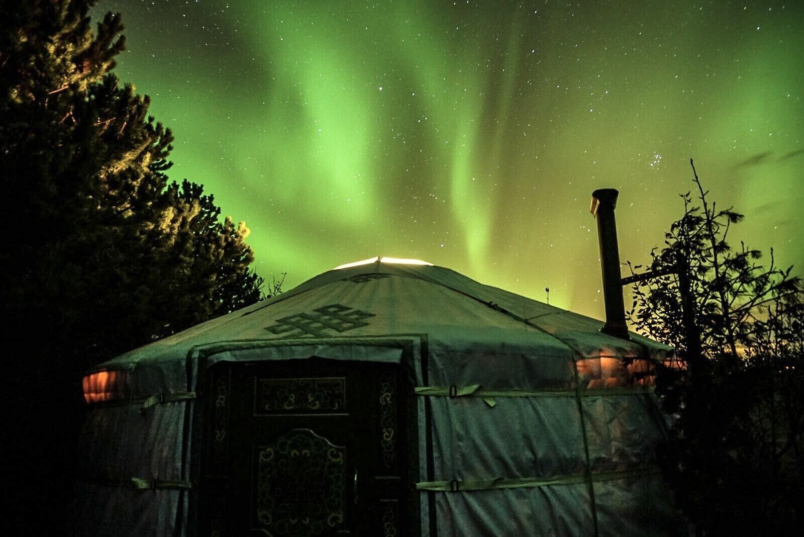 A yurt with a starry night sky and aurora borealis.