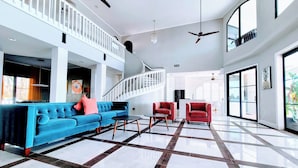 Un vaste espace de vie comprenant un canapé bleu, des fauteuils rouges, une table basse noire et un escalier blanc.