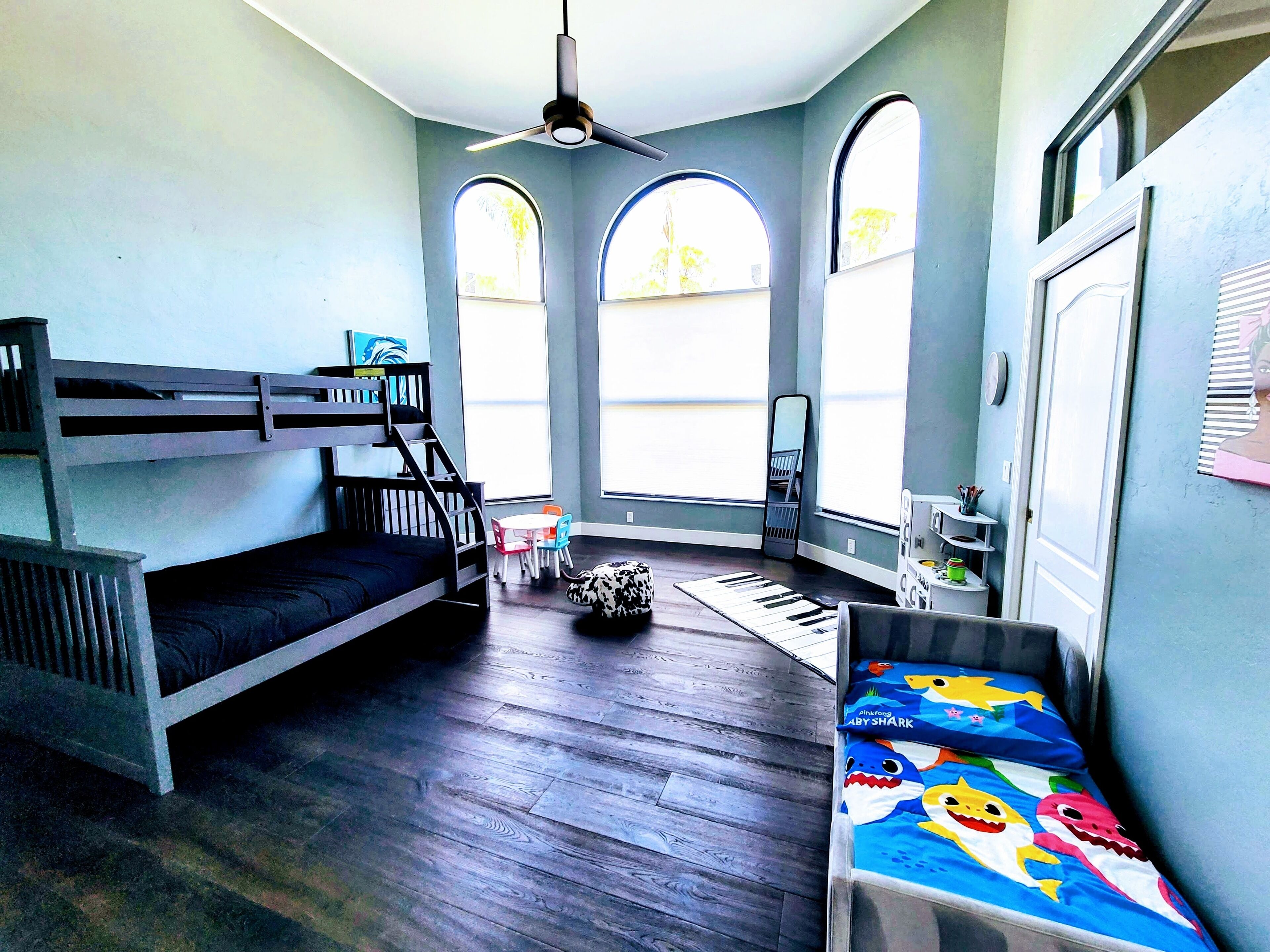 A room with a bunk bed, a ceiling fan, a small table with chairs, and a window with a view.