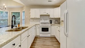 Una cocina con armarios blancos, un lavamanos doble, una estufa y un refrigerador.