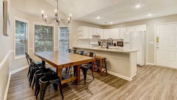 Una cocina amplia con una mesa de comedor de madera, armarios blancos y una isla integrada con un lavamanos.