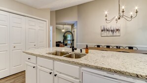 Una cocina con gabinetes blancos, encimera de granito, pileta de acero inoxidable y candelabro.