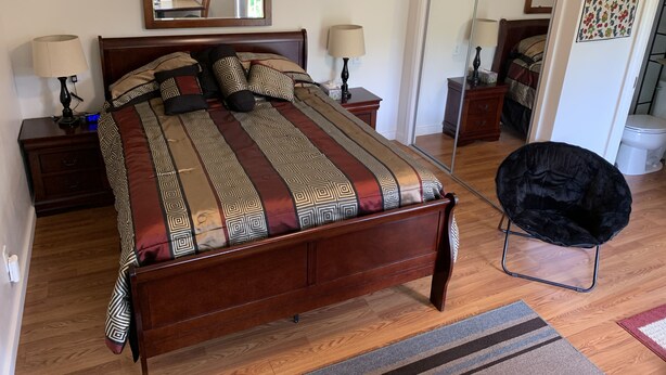 A bedroom with a large bed, two bedside tables, a mirror, and a black chair.