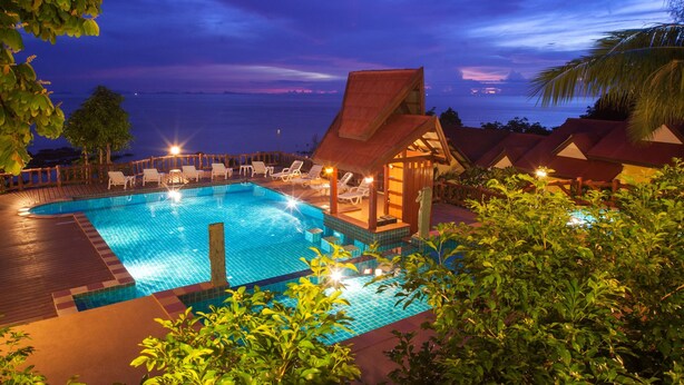 A pool area with lounge chairs and a small building, surrounded by greenery and overlooking the sea. - Zama Resort (Ko Pha-ngan)