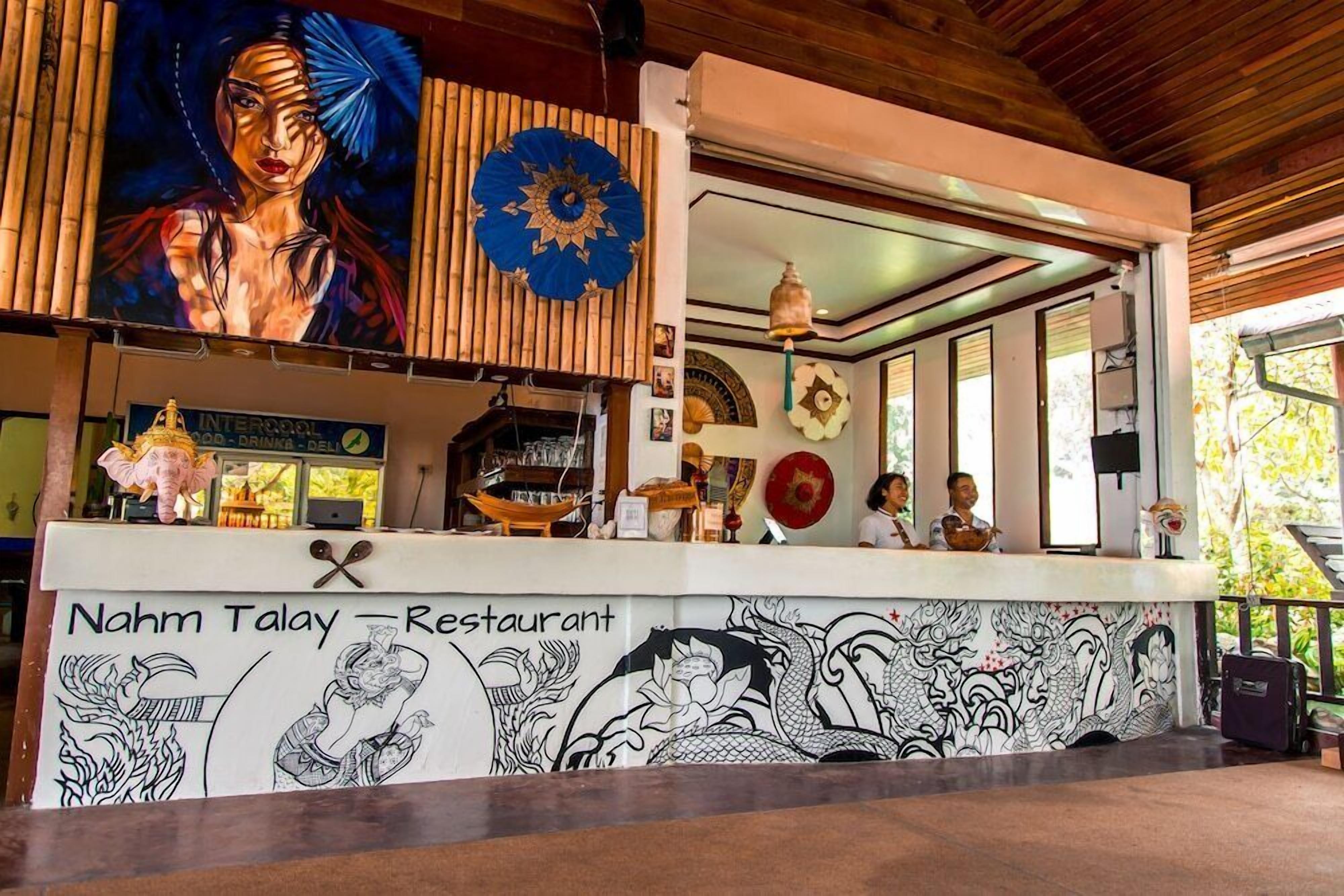 A restaurant with a counter, a mural, and a sign reading "Nahm Talay Restaurant".