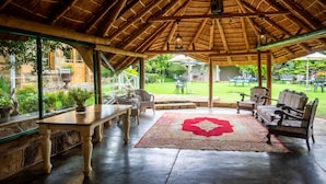 A covered outdoor seating area with a wooden ceiling, a red patterned rug, and potted plants. - Fouriesburg Country Inn (Fouriesburg)