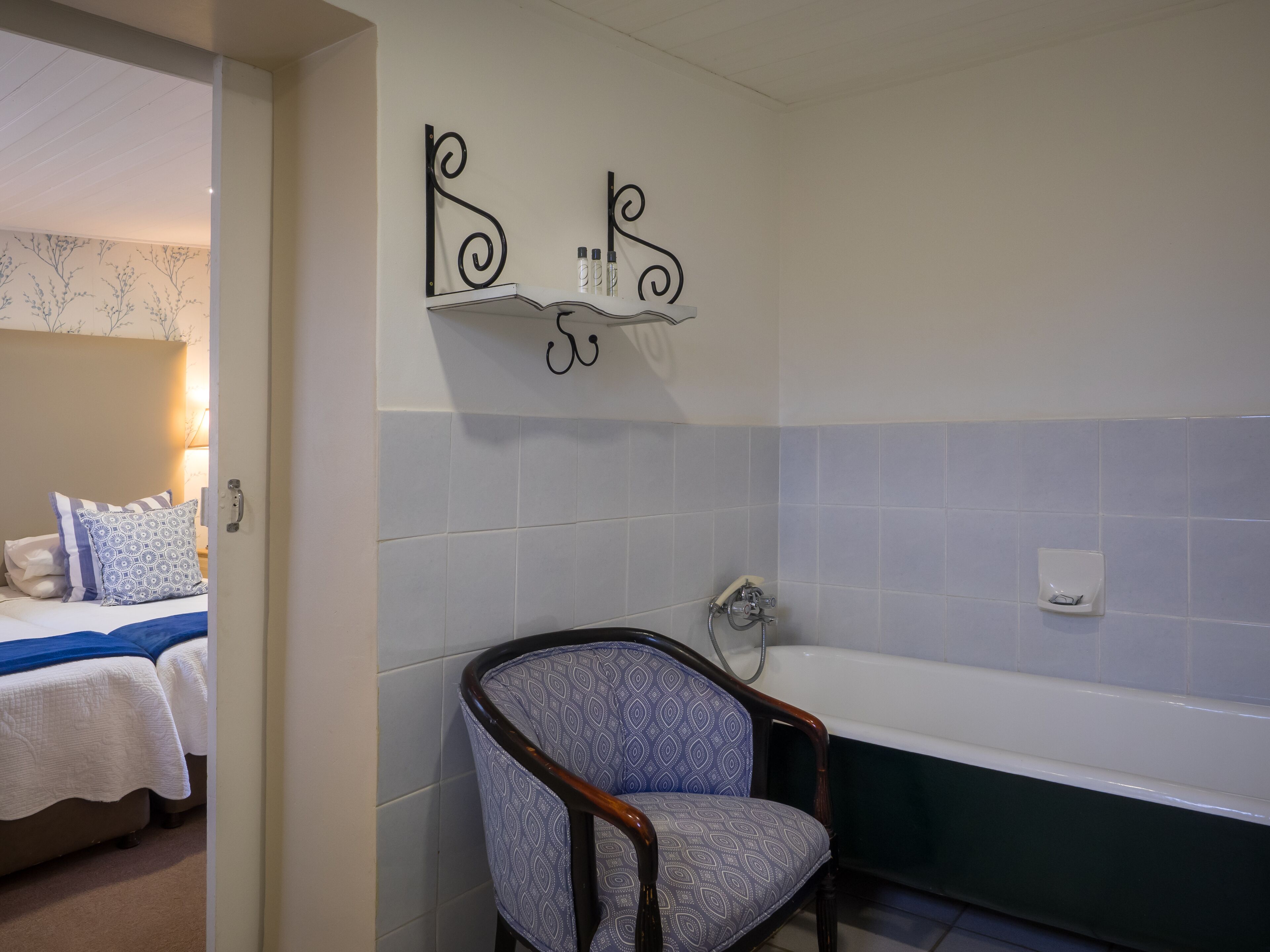 A bathroom with a bathtub, a chair, and a bed with patterned pillows.