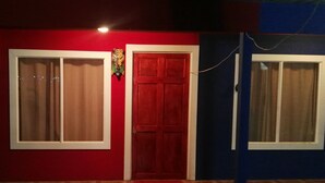 A building with a red door and windows, wooden flooring, and a small plant in front.
