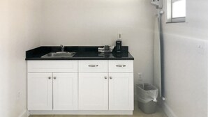 A small kitchenette with a black countertop, white cabinets, a sink, a coffee maker, and a trash can. - Everglades City Motel - Queen Room, 2 Beds, Kitchenette (Everglades City)