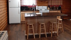 Une cuisine compacte aux murs en bois, équipée d’un réfrigérateur, d’une cuisinière, d’un évier et d’un coin bar avec des tabourets.
