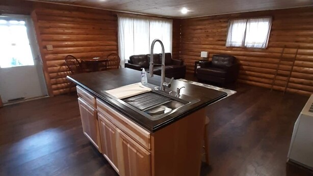 L’intérieur d’une cabane en rondins comprend un îlot de cuisine, un plancher en bois et un coin repas avec un canapé et des fauteuils.