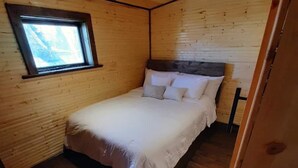 Une petite chambre à coucher accueillante, avec un plafond et des murs en bois, un lit simple avec des oreillers et une fenêtre laissant entrer la lumière naturelle.
