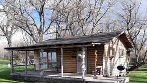 Une cabane en rondins avec un porche, un barbecue et une petite terrasse.
