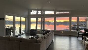 A spacious living room with a large window overlooking a lake, a sofa, and a dining area.