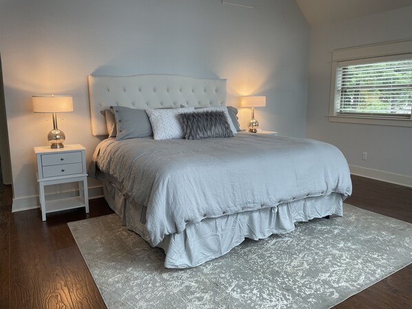 A bedroom with a large bed, two bedside tables, and a window with blinds. - Amazing Lake Home right on the water with breathtaking views! (Hot Springs)