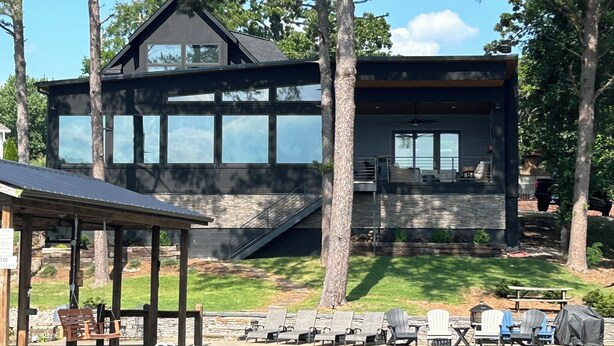 Une maison moderne dotée de grandes fenêtres, d’un quai et d’un espace de détente extérieur au bord de l’eau.