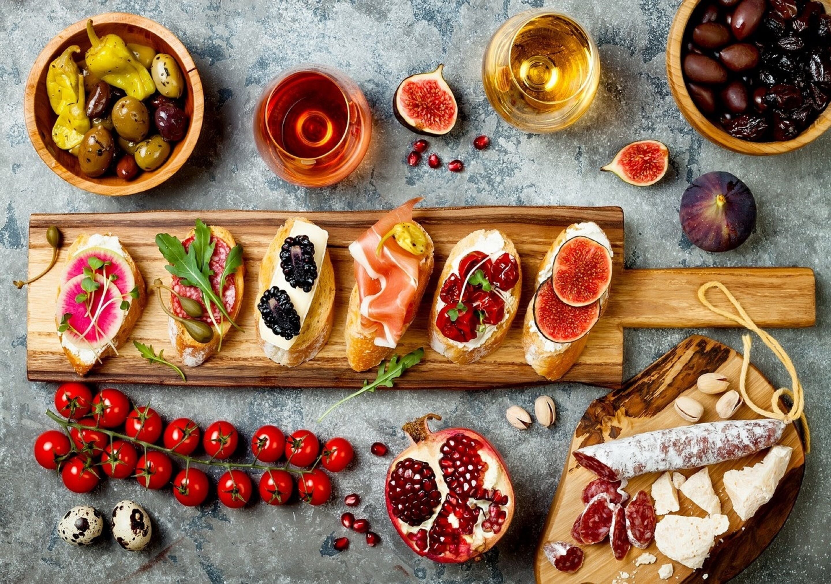 A variety of food items including olives, figs, pomegranate, and cheese on wooden boards.