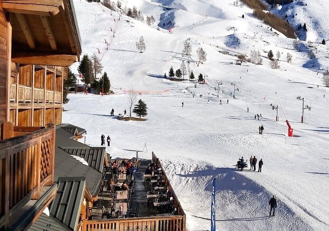 A wooden building with a balcony overlooking a snowy ski slope.