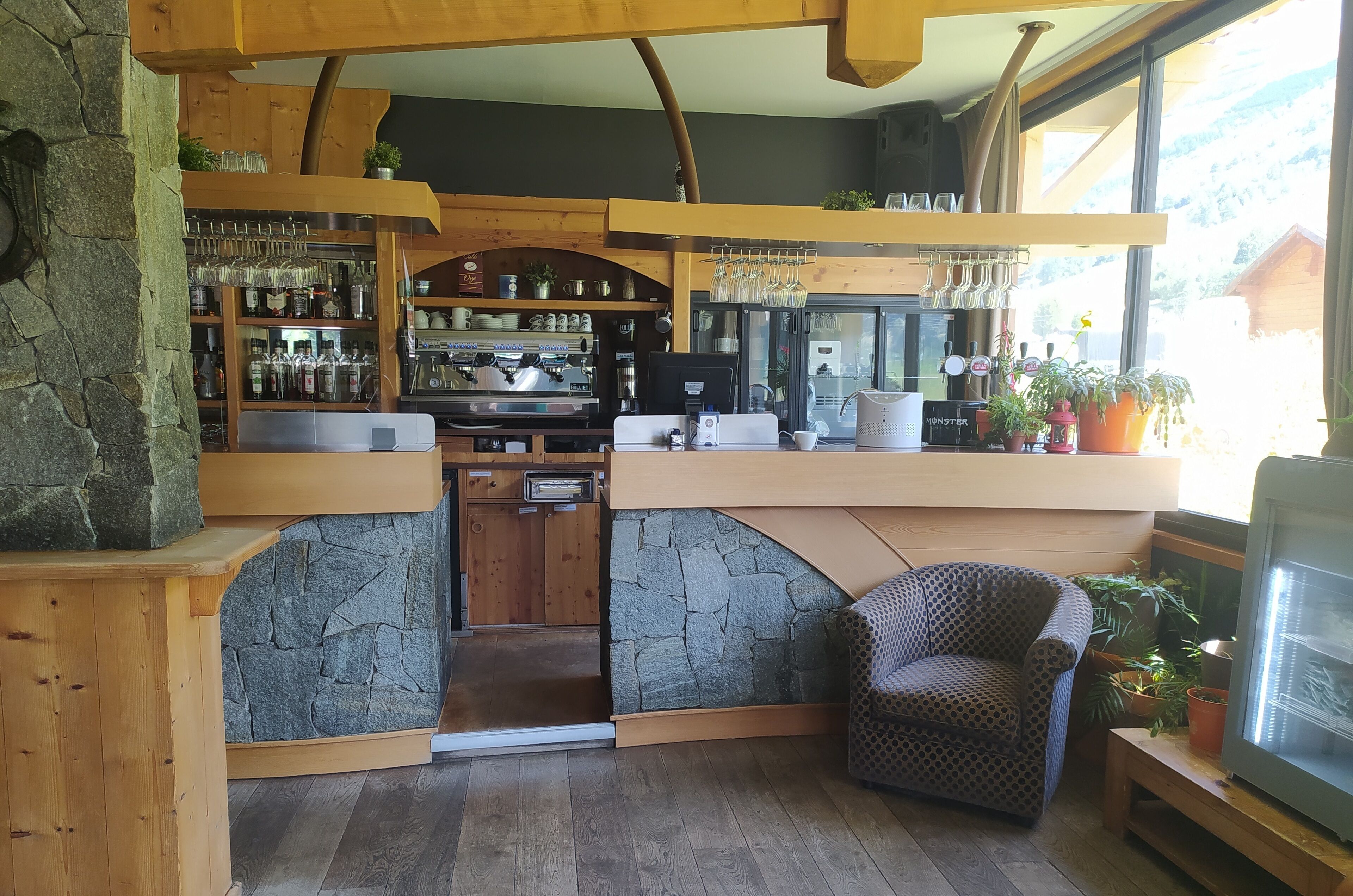 A cozy bar area with a stone accent wall, wooden furniture, and a seating area with a patterned chair.