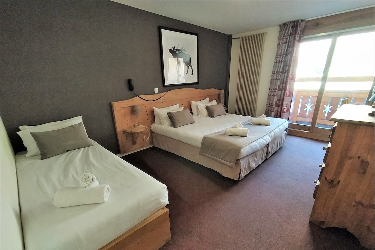 A hotel room with two single beds, a wooden headboard, a framed picture on the wall, and a view of the outdoors through a window.