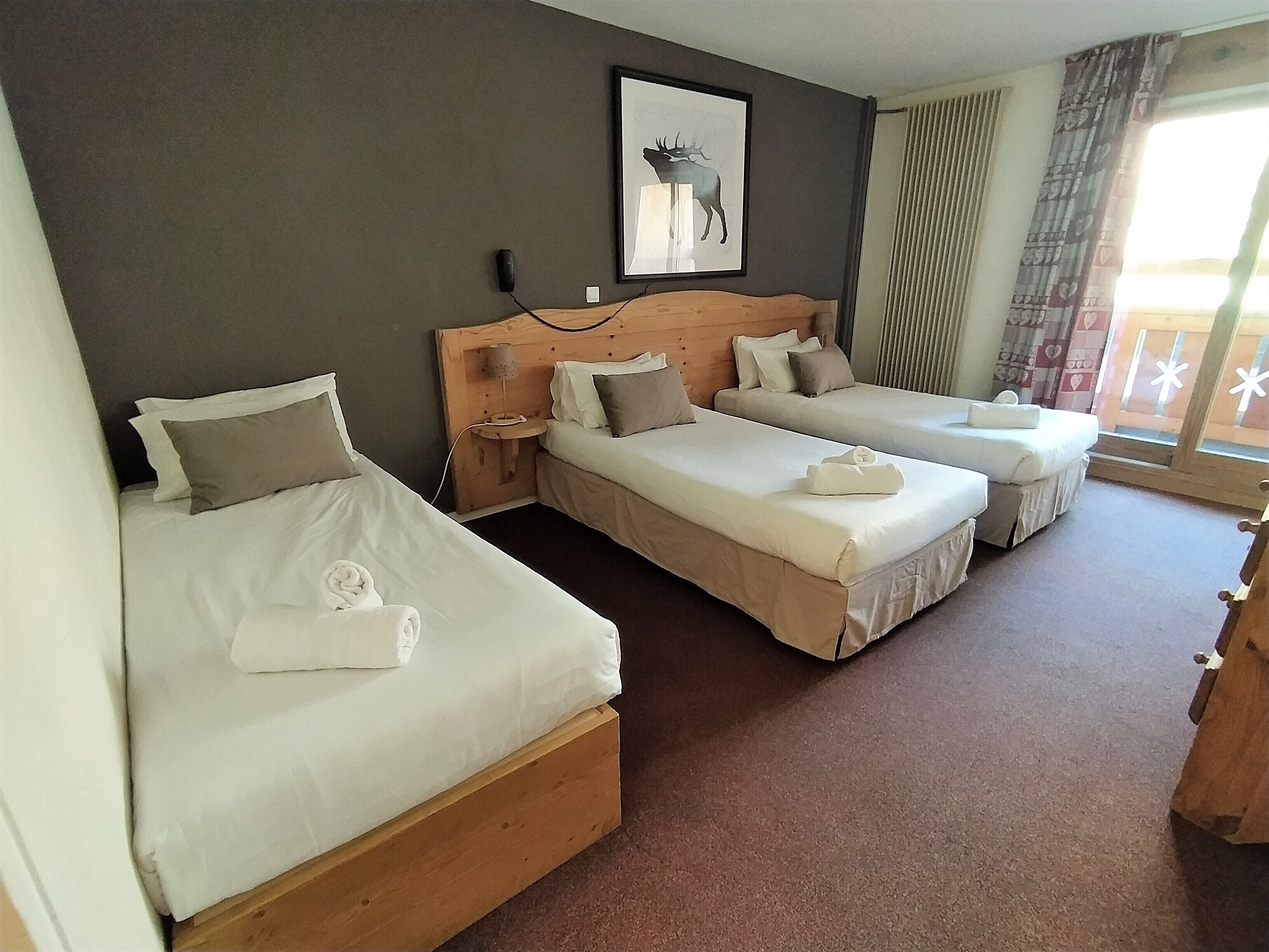 Ett hotellrum med två separata sängar, en sänggavel i trä, en inramad tavla på väggen och ett fönster med gardiner.
