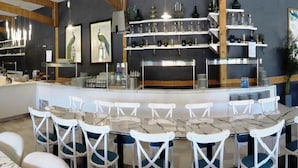 Eine Bar mit weißen Stühlen und einem Marmortisch, Regalen für Gläser und gerahmten Bildern an der Wand.
