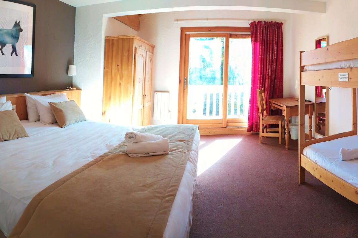 A hotel room with a large bed, a smaller bed, a desk, and a chair. There is a sliding glass door leading to an outdoor area.