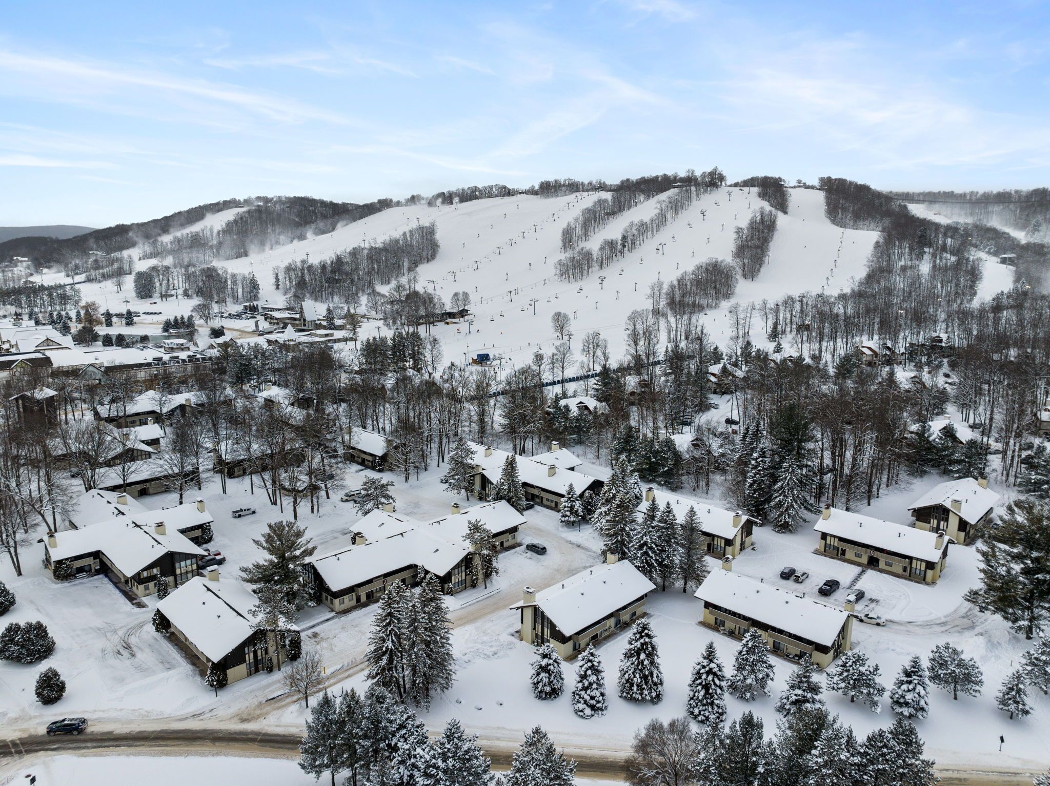 Une station de ski enneigée, composée de plusieurs bâtiments, dont des chalets et un refuge, entourée d’arbres et bordée d’une piste de ski.