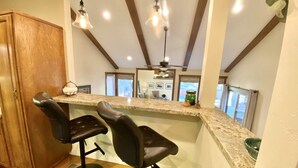 A kitchen with a marble countertop, two black bar stools, a wooden cabinet, and pendant lighting. - Prime Skier's Pad for a Magical Vacation (Cottonwood Heights)