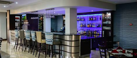 A modern bar area with a curved counter, bar stools, and a variety of bottles and glasses.