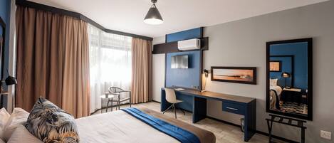 Una habitación de hotel con cama, escritorio, silla y un espejo grande.
