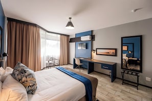 A hotel room with a bed, desk, chair, and a large mirror.