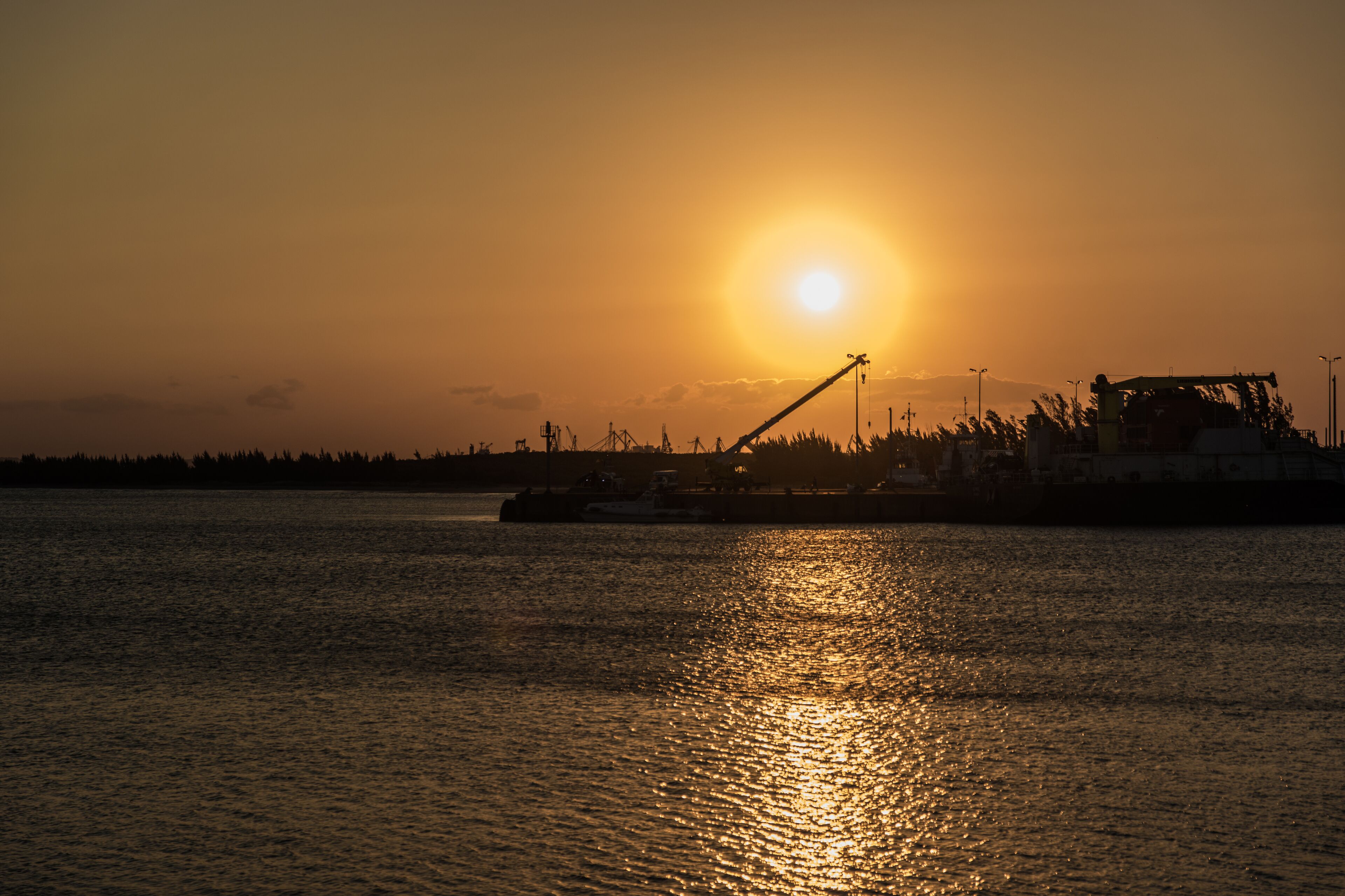 A sunset over a body of water with industrial structures in the background.