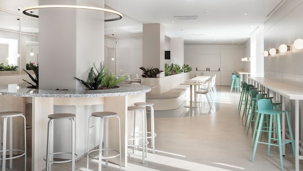 A modern bar area with a curved counter, white stools, and green bar stools.