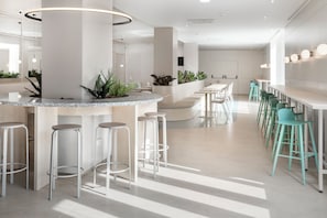 Uma área de bar moderna com balcão curvo, banquetas brancas e banquetas verdes.