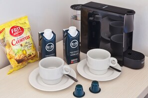 A breakfast setup with two white cups, a bag of Frit Ravich Caseras chips, two B&B Hotels milk cartons, and a coffee maker.