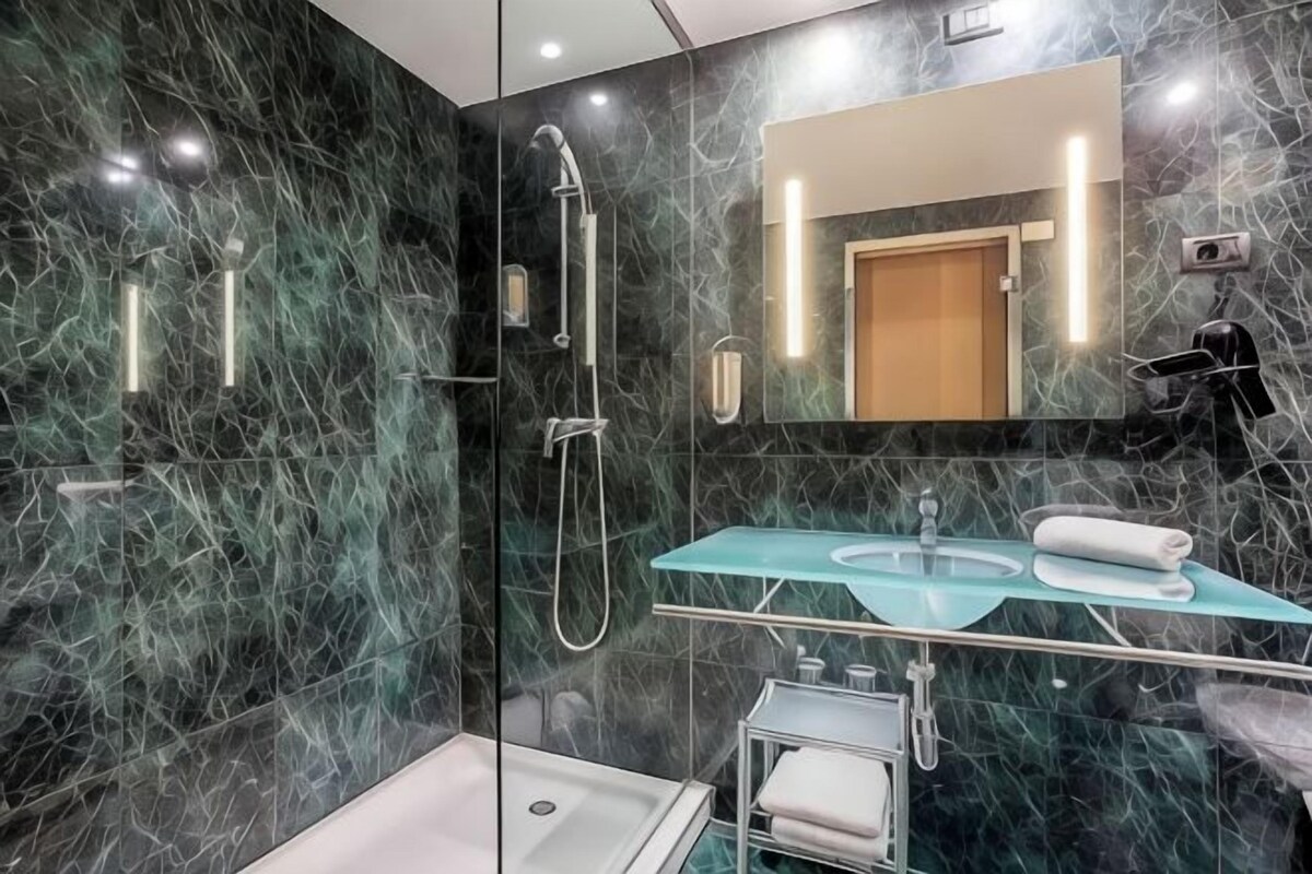 Un baño moderno con lavamanos de vidrio, ducha e inodoro.